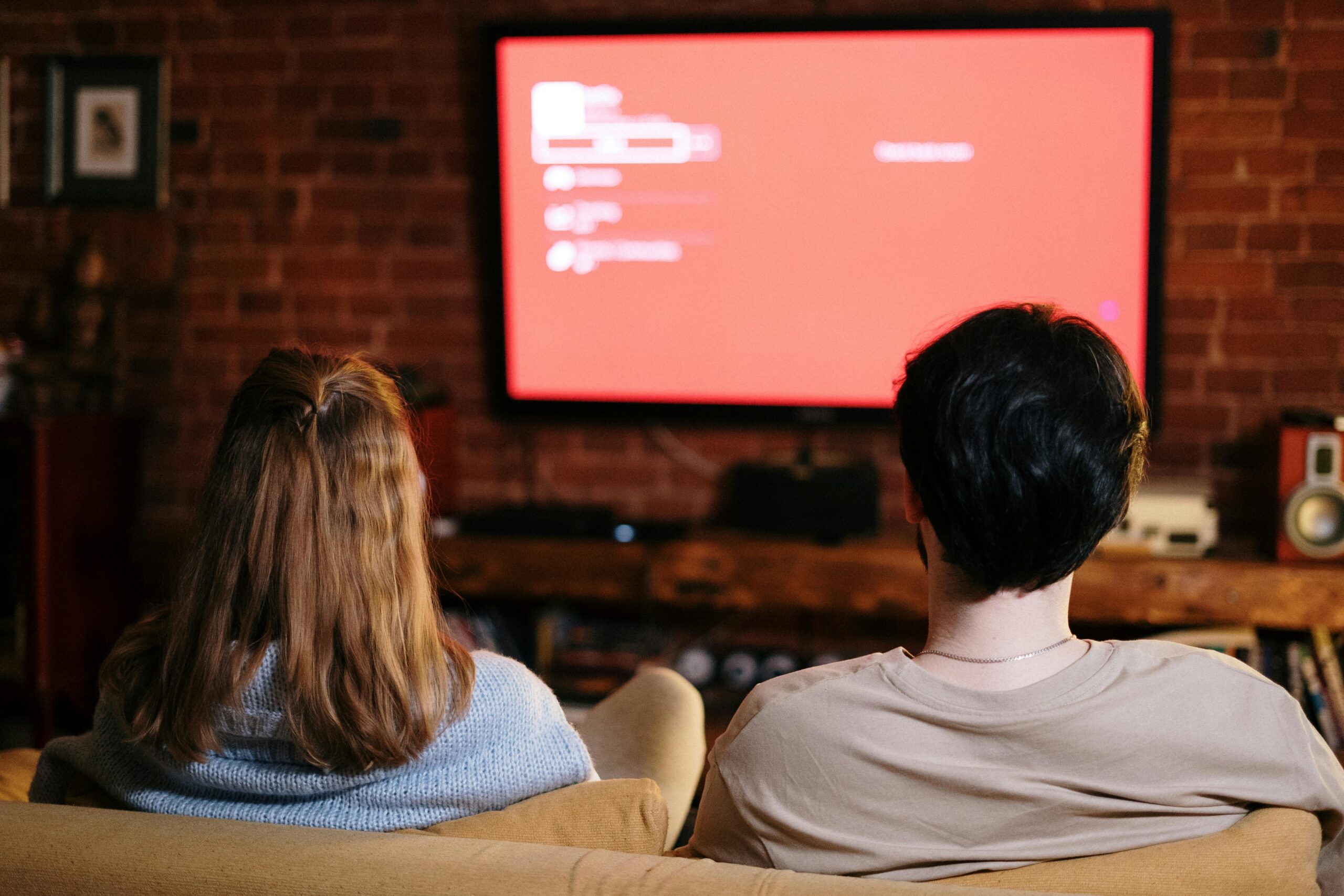 A couple watches TV together in a cozy brick-walled living room on a sofa.